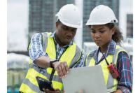 Two constructions workers with Red CSCS card examining a design blueprint.