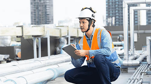 Man squats with tablet beside piping